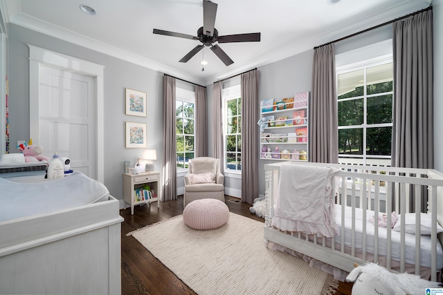 bedroom with ceiling fan, crown molding, dark hardwood / wood-style floors, and a crib