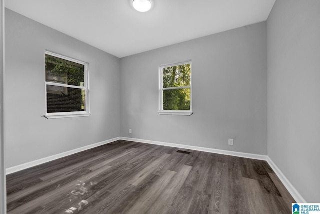 unfurnished room featuring visible vents, dark wood-style flooring, and baseboards