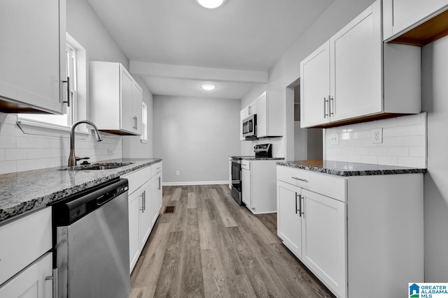 kitchen with a sink, light wood-style floors, dark stone countertops, backsplash, and appliances with stainless steel finishes