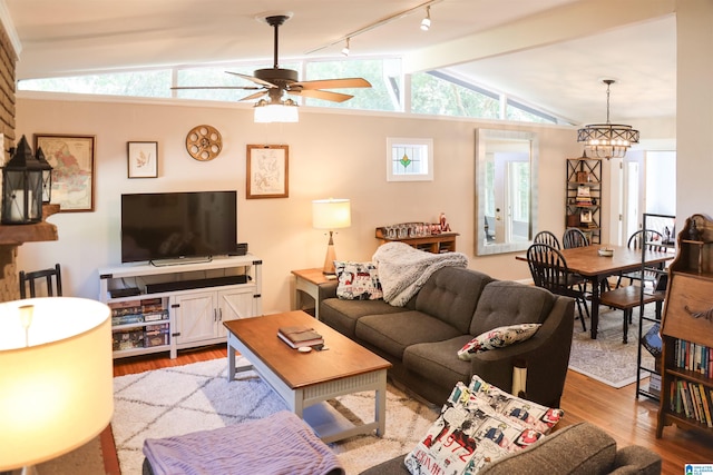 living room featuring rail lighting, vaulted ceiling with beams, light wood-type flooring, and ceiling fan with notable chandelier