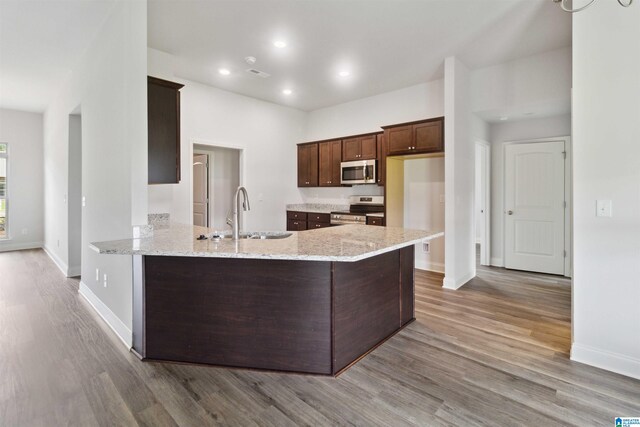 kitchen with light stone counters, sink, kitchen peninsula, stainless steel appliances, and light wood-type flooring