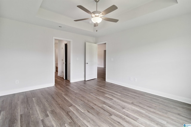 spare room with a tray ceiling, light wood-type flooring, and ceiling fan