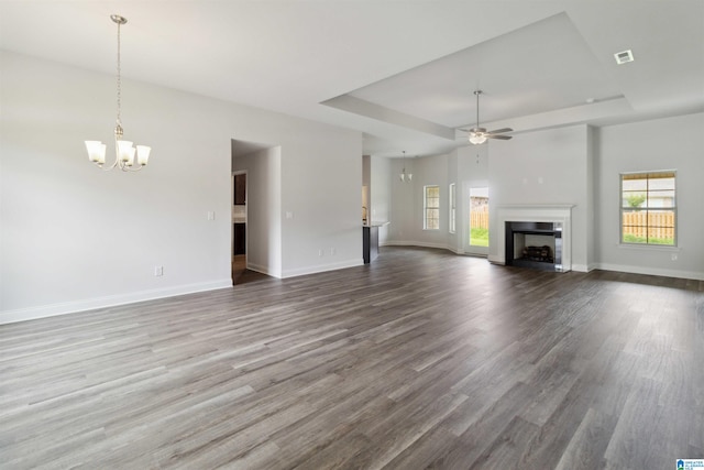 unfurnished living room featuring ceiling fan with notable chandelier, a tray ceiling, and hardwood / wood-style floors