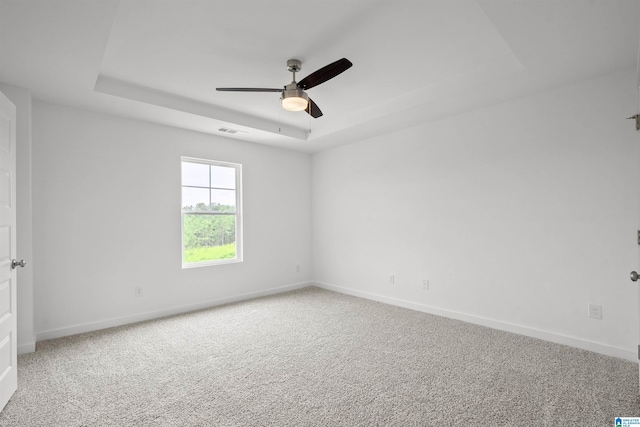 spare room with ceiling fan, a raised ceiling, and carpet flooring