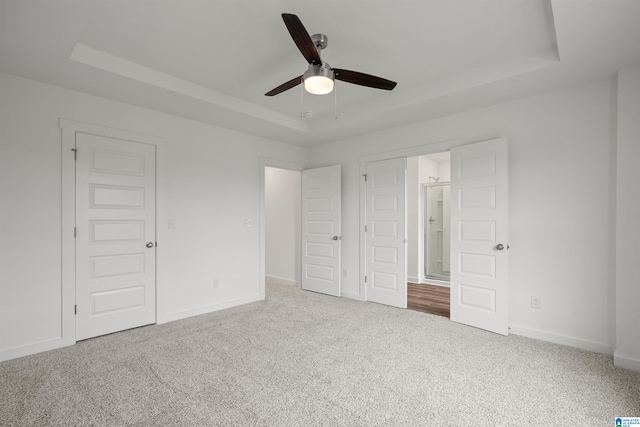 unfurnished bedroom with ceiling fan, a tray ceiling, and carpet flooring