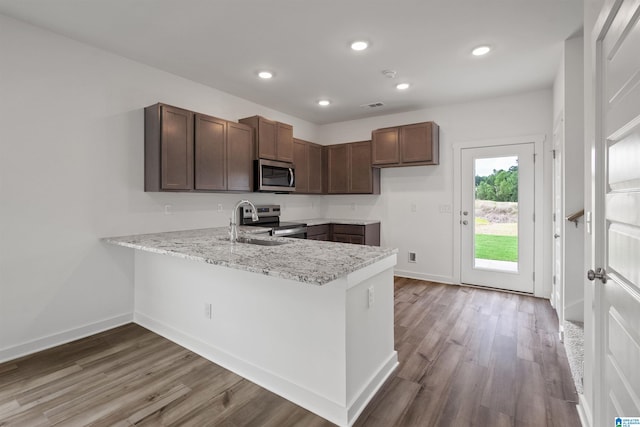 kitchen with sink, kitchen peninsula, wood-type flooring, appliances with stainless steel finishes, and light stone countertops