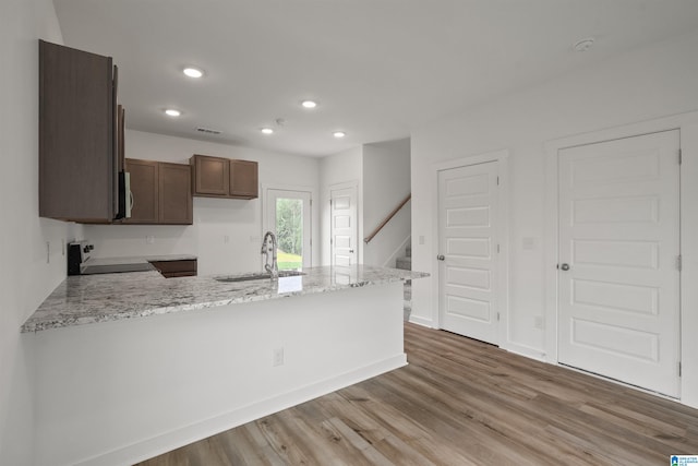 kitchen with light wood-type flooring, light stone counters, black stove, sink, and kitchen peninsula