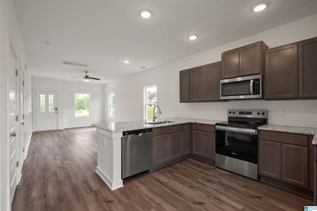 kitchen featuring dark hardwood / wood-style flooring, light stone countertops, sink, stainless steel appliances, and kitchen peninsula