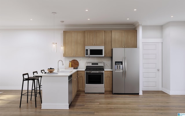 kitchen with sink, kitchen peninsula, decorative light fixtures, appliances with stainless steel finishes, and a breakfast bar