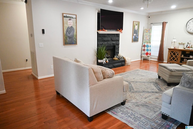 living room with wood-type flooring, crown molding, and a stone fireplace