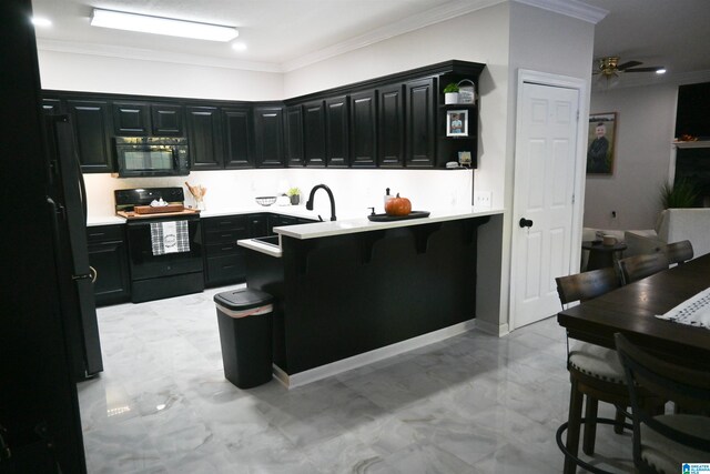 kitchen with ornamental molding, black appliances, ceiling fan, and a kitchen breakfast bar