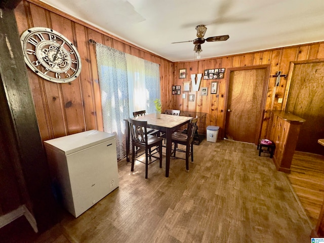 dining space featuring ceiling fan, wooden walls, and wood-type flooring