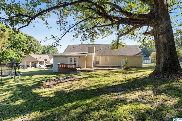 back of property featuring a wooden deck, a trampoline, and a lawn