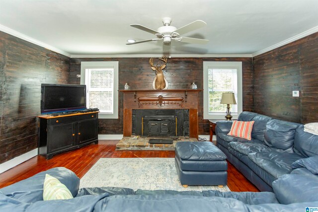 living room with crown molding, ceiling fan, dark hardwood / wood-style flooring, and a wood stove