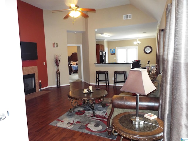 living room with lofted ceiling, dark wood-type flooring, a tile fireplace, and ceiling fan