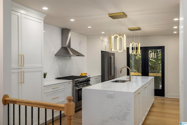 kitchen featuring pendant lighting, sink, premium appliances, wall chimney range hood, and white cabinetry