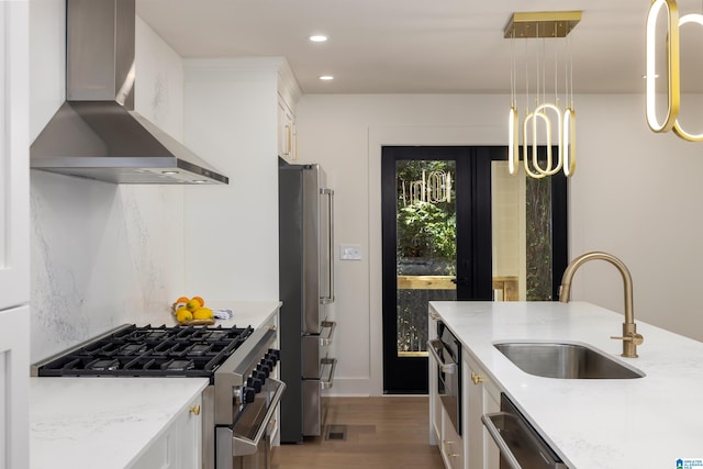 kitchen with white cabinets, sink, decorative light fixtures, wall chimney range hood, and appliances with stainless steel finishes