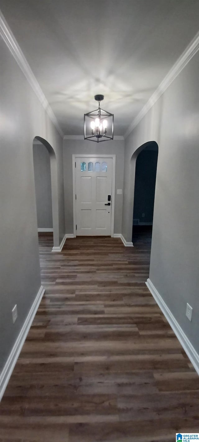 foyer entrance featuring ornamental molding, dark wood-type flooring, and an inviting chandelier