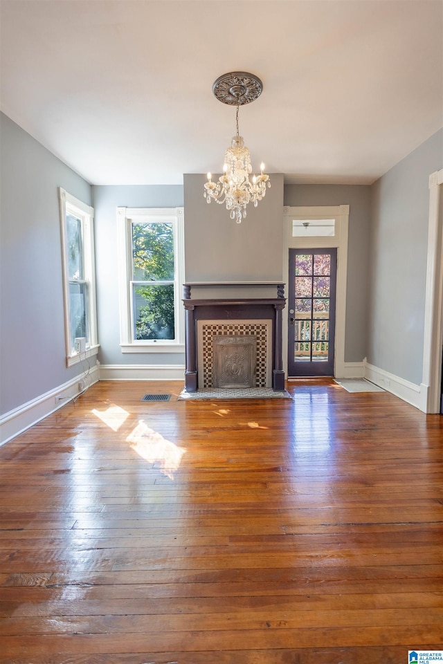 unfurnished living room with a healthy amount of sunlight, a tile fireplace, hardwood / wood-style floors, and a chandelier