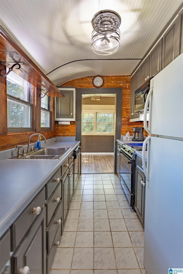 kitchen with wood walls, light tile patterned floors, sink, black appliances, and vaulted ceiling