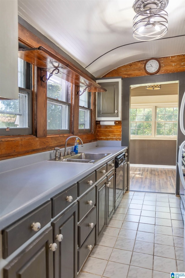 kitchen with wooden walls, sink, light tile patterned floors, and dishwasher