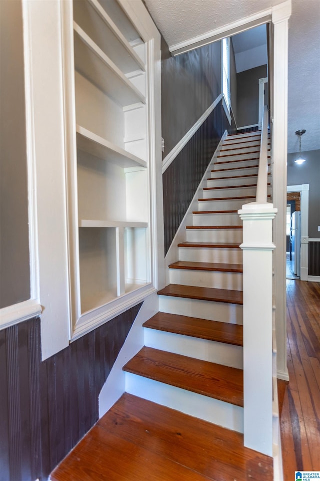 stairs with a textured ceiling, wooden walls, and hardwood / wood-style floors