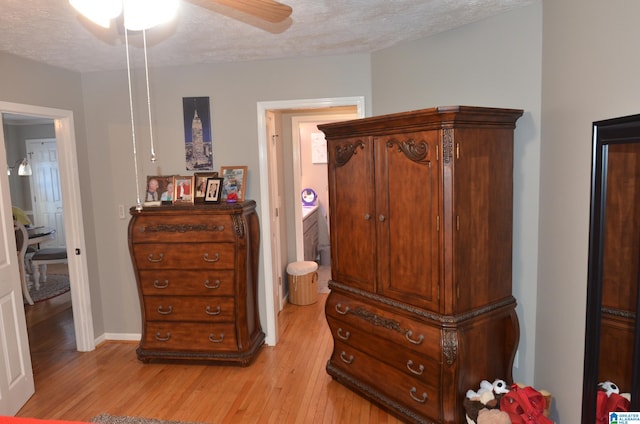 bedroom with ceiling fan, ensuite bath, light hardwood / wood-style flooring, and a textured ceiling