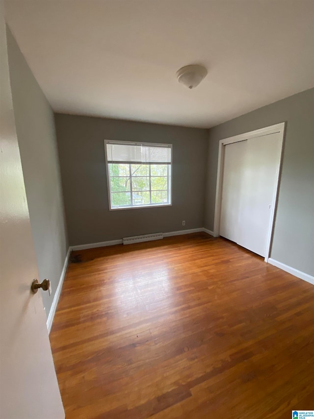 unfurnished bedroom featuring a closet, a baseboard heating unit, and wood-type flooring