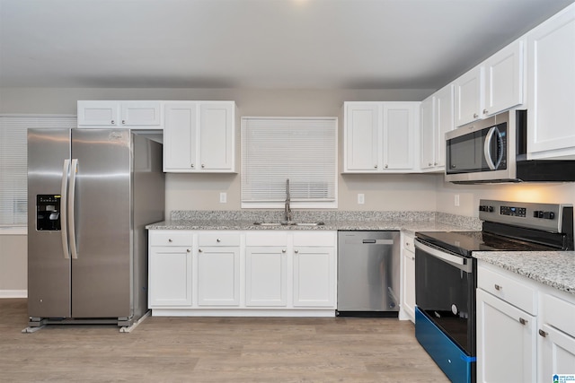 kitchen with light hardwood / wood-style flooring, sink, stainless steel appliances, light stone countertops, and white cabinetry