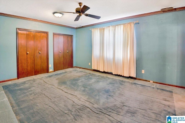 unfurnished bedroom with two closets, carpet, ceiling fan, a textured ceiling, and ornamental molding