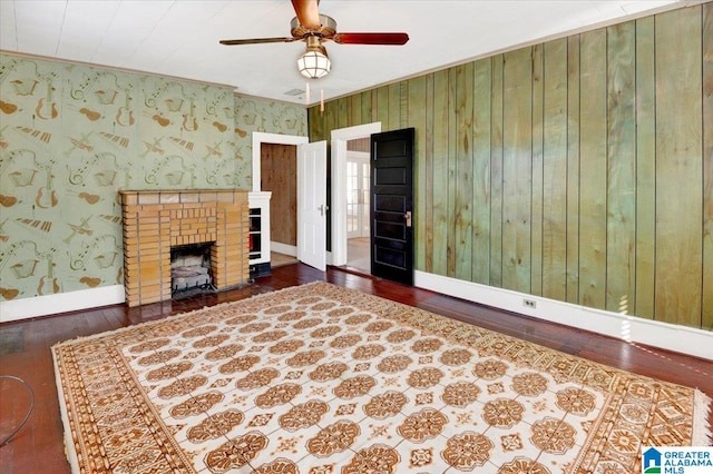 unfurnished living room with ceiling fan, a fireplace, dark hardwood / wood-style floors, and wood walls