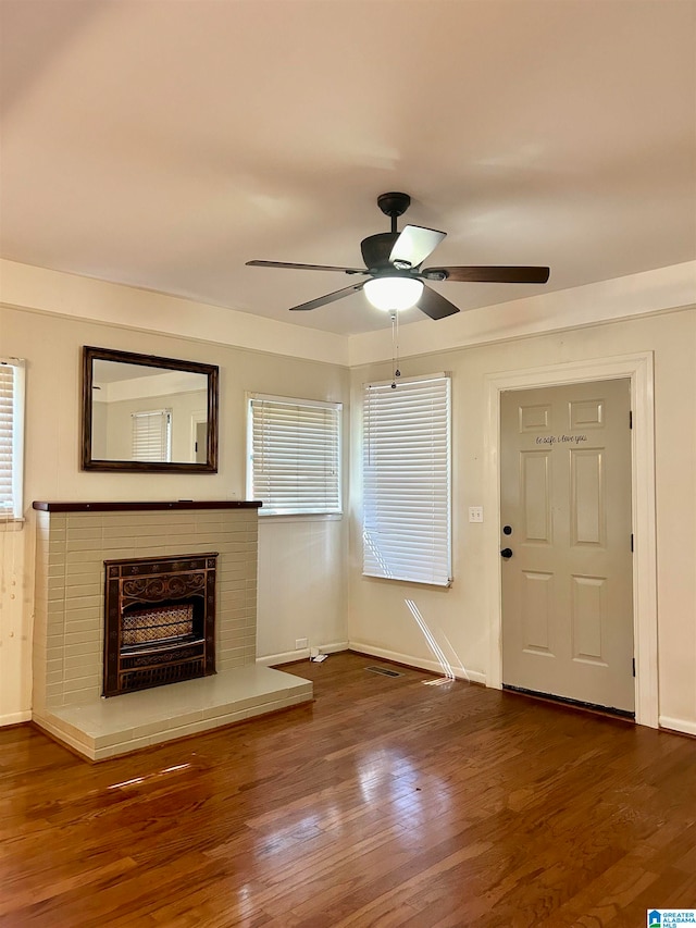 unfurnished living room featuring dark hardwood / wood-style floors, ceiling fan, and a brick fireplace