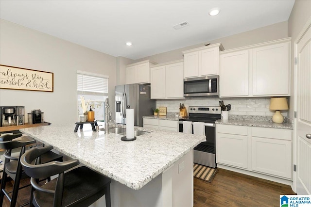 kitchen featuring white cabinetry, appliances with stainless steel finishes, a kitchen breakfast bar, an island with sink, and dark wood-type flooring