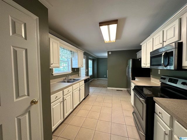 kitchen with white cabinets, light tile patterned floors, ornamental molding, sink, and stainless steel appliances