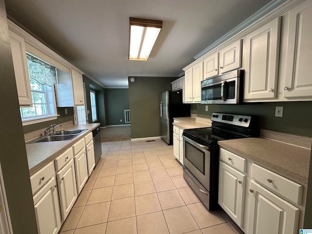 kitchen with ornamental molding, sink, white cabinets, light tile patterned floors, and appliances with stainless steel finishes