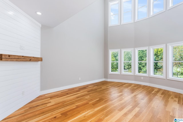 unfurnished living room with a high ceiling, wooden walls, light hardwood / wood-style floors, and a healthy amount of sunlight