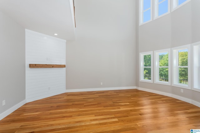 unfurnished living room with wood walls, a towering ceiling, and light hardwood / wood-style floors