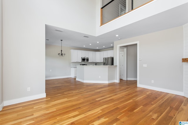 unfurnished living room featuring a notable chandelier, a towering ceiling, and light hardwood / wood-style floors