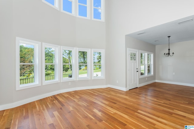 unfurnished living room with a high ceiling, a notable chandelier, and light wood-type flooring