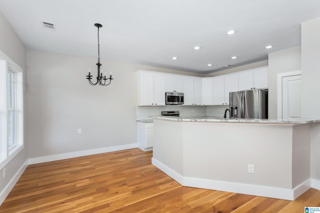 kitchen featuring a chandelier, light hardwood / wood-style flooring, light stone counters, stainless steel appliances, and white cabinetry