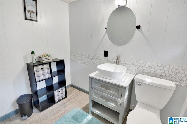 bathroom with hardwood / wood-style floors, wooden walls, toilet, and vanity