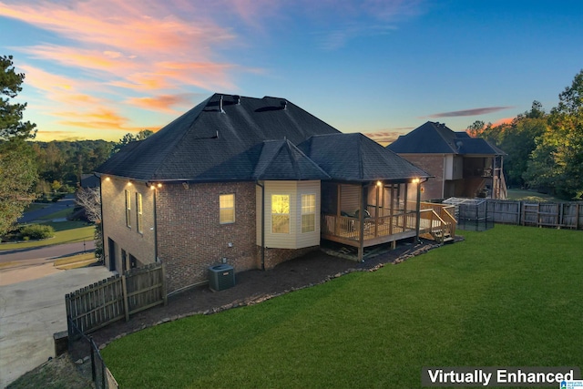 back house at dusk with a yard, a wooden deck, and central AC unit