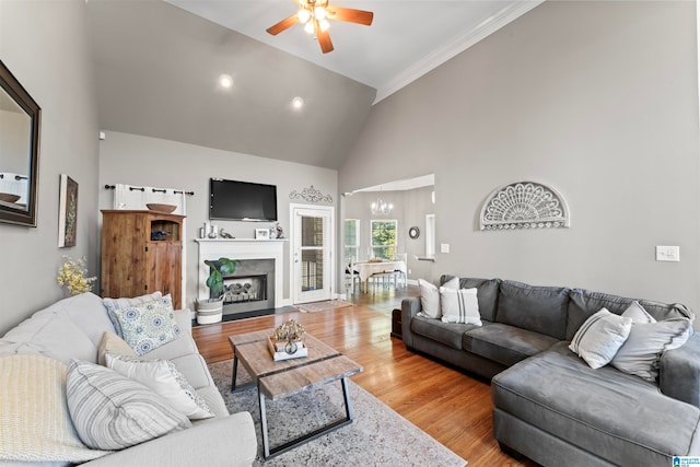 living room with crown molding, high vaulted ceiling, wood-type flooring, and ceiling fan with notable chandelier