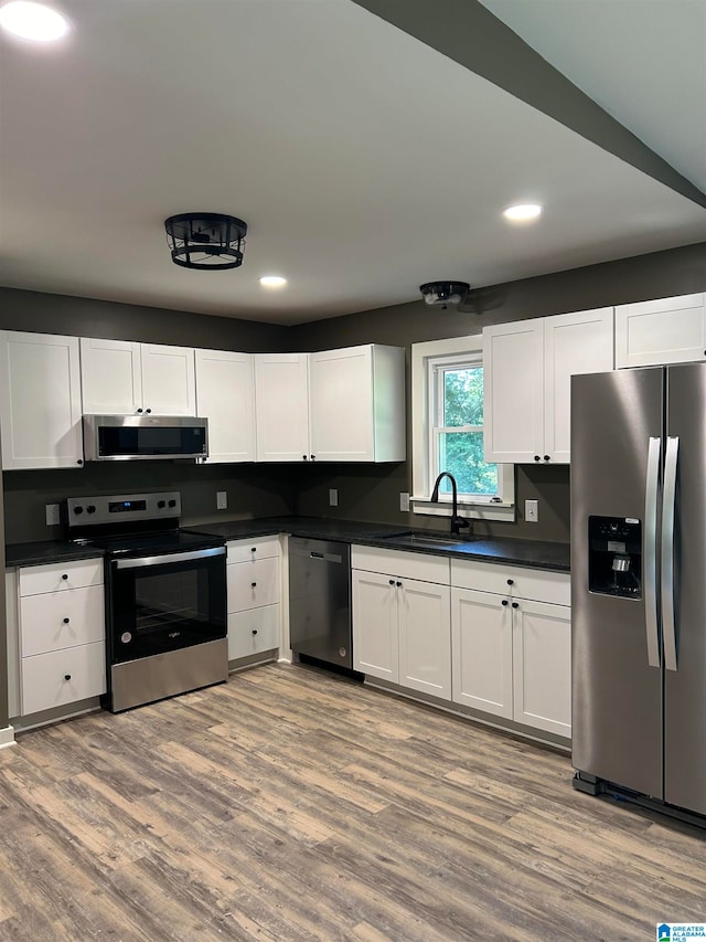 kitchen with hardwood / wood-style floors, sink, stainless steel appliances, and white cabinets