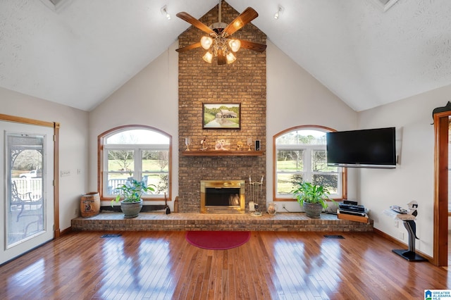 unfurnished living room with a brick fireplace, ceiling fan, hardwood / wood-style floors, high vaulted ceiling, and a textured ceiling