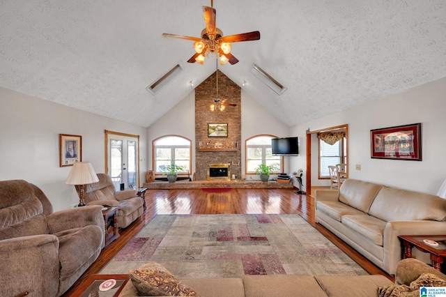 living room featuring high vaulted ceiling, ceiling fan, wood-type flooring, a fireplace, and a textured ceiling