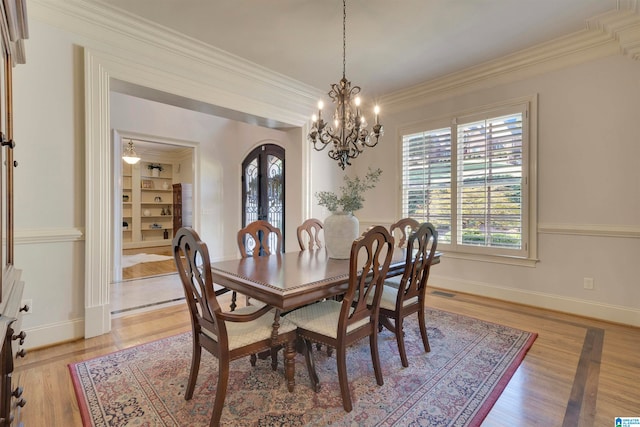 dining space with ornamental molding, built in shelves, a chandelier, and light hardwood / wood-style flooring