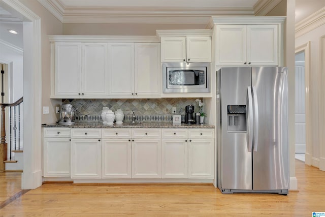 kitchen with white cabinets, stainless steel appliances, light wood-type flooring, and dark stone counters