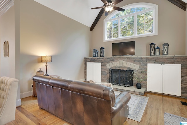 living room with high vaulted ceiling, ceiling fan, a stone fireplace, light hardwood / wood-style floors, and beam ceiling