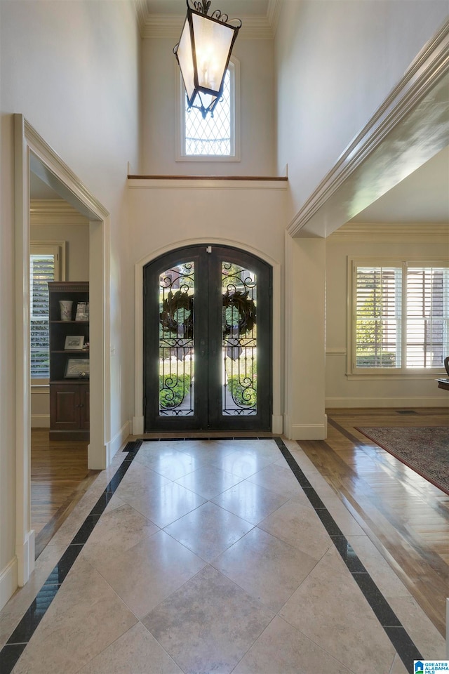 foyer entrance with french doors, light wood-type flooring, crown molding, and a high ceiling